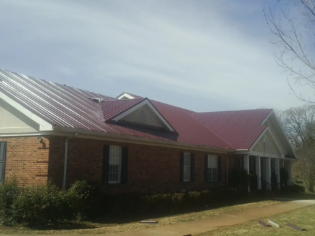 Red metal roof with gabled entries on a long brick building, from a Hail Damage Roof Repair job in Greens Fork