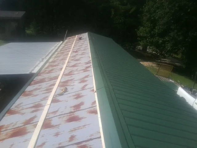 Old rusted panels beside newly installed green metal roofing — Wind Damage Roof Repair by Roofing Brothers in Greens Fork
