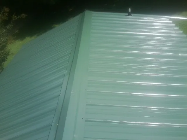 New green metal panels meeting at the ridge of a roof — Flat Roof Repair work by our crew in Greens Fork