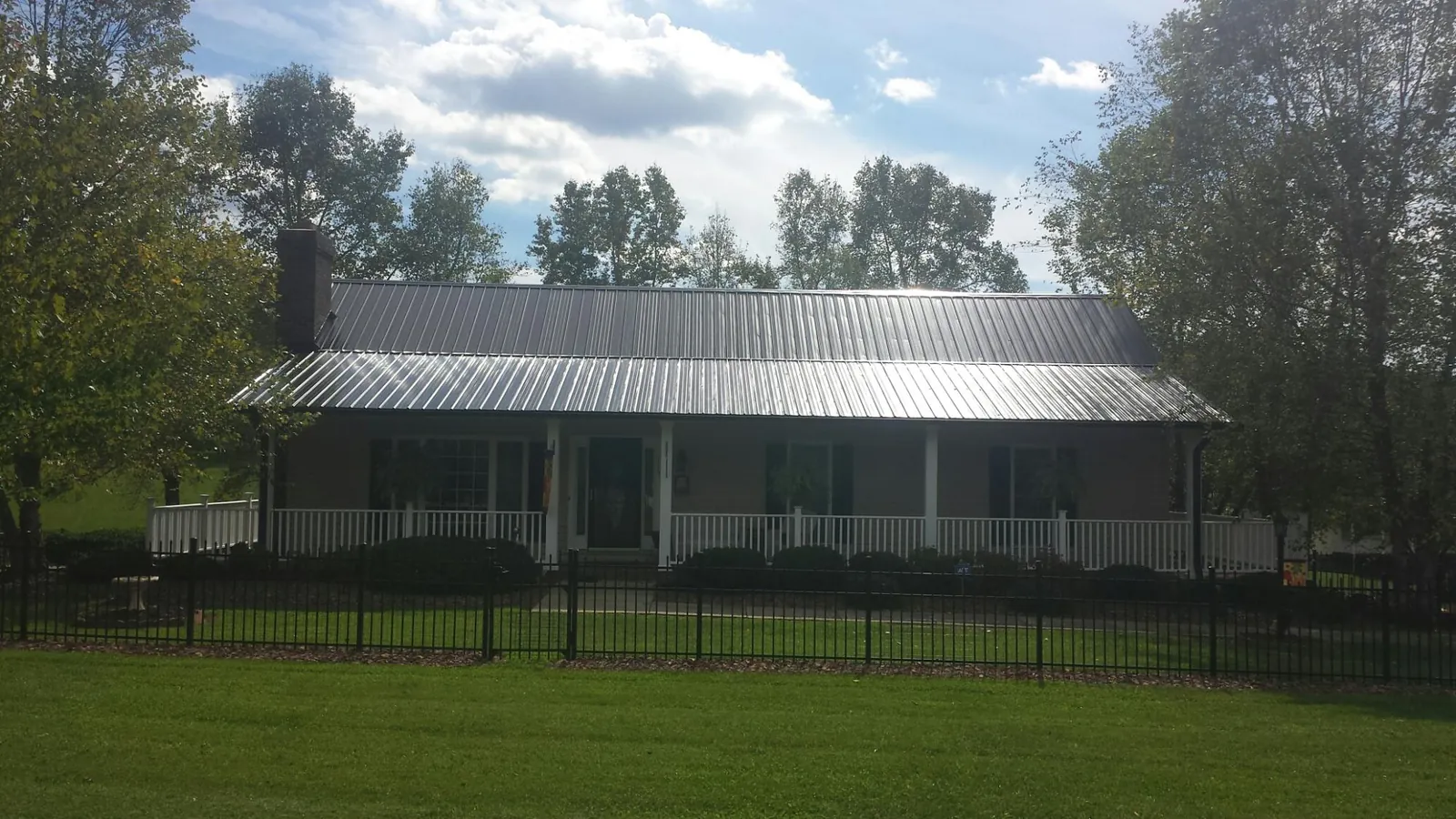 Gray metal roof on a brick ranch with a full width front porch — Gutter Guard Installation work by our crew in Greens Fork