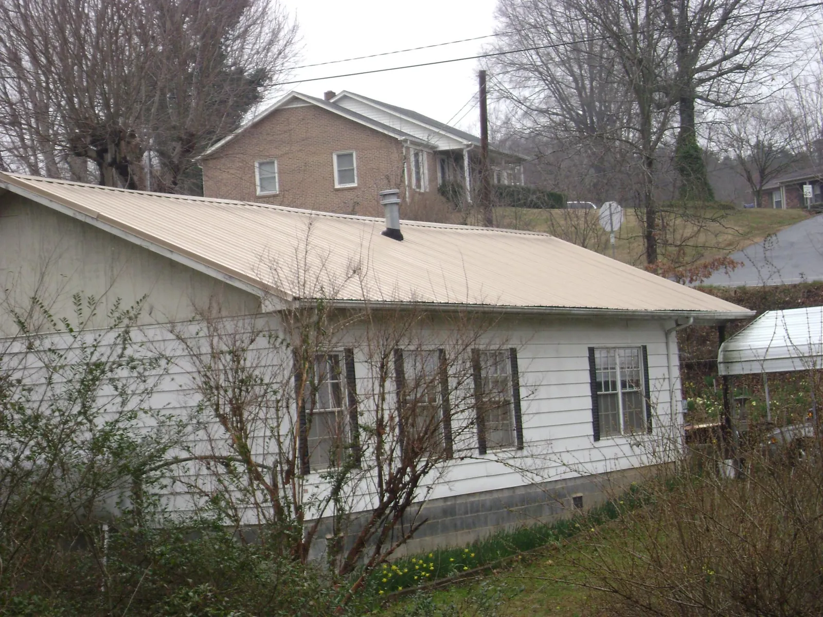Tan metal roof on a white sided house set into a hillside — Commercial Roofing by Roofing Brothers in Greens Fork