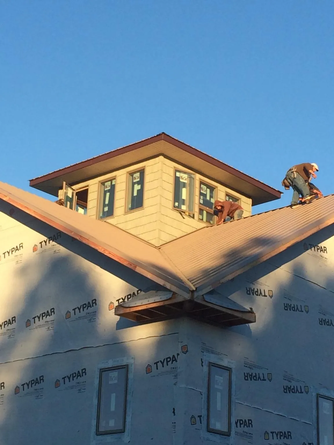 Roofers working around a rooftop cupola on a new metal roof at sunset — Roof Waterproofing in Greens Fork by Roofing Brothers